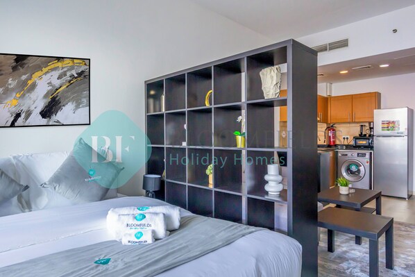 A modern hotel room with a large bed, a built-in wardrobe, a small kitchen area, and a bathroom.