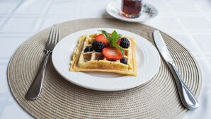 A breakfast setting with a plate of waffles topped with berries and a mint leaf, accompanied by a cup of tea and cutlery on a table with a placemat. - Bath Street Inn B & B, Santa Barbara (Santa Barbara)
