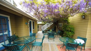 An outdoor patio with a wooden deck, green metal chairs, and tables. There is a staircase leading to an upper level. - Bath Street Inn B & B, Santa Barbara (Santa Barbara)