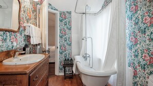 A bathroom with a wooden vanity, a white sink, a clawfoot bathtub, and floral wallpaper. - Bath Street Inn B & B, Santa Barbara (Santa Barbara)