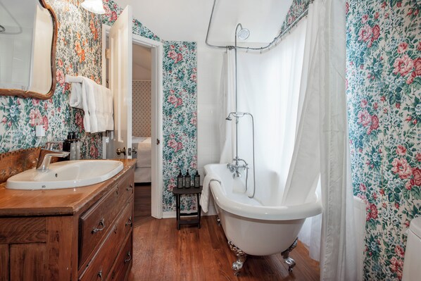 A bathroom with a wooden vanity, a white sink, a clawfoot bathtub, and floral wallpaper. - Bath Street Inn B & B, Santa Barbara (Santa Barbara)