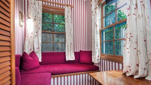 Une pièce chaleureuse avec un mur à rayures, un banc en bois et un coin salon confortable agrémenté de coussins et de rideaux à motifs floraux.