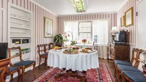 Un coin repas comprenant une table ronde, des chaises, un tapis à motifs et une bibliothèque où sont exposés des objets en verre.
