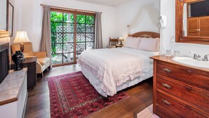 A bedroom with a large bed, a wooden dresser, a nightstand, a lamp, a window with curtains, and a view of greenery outside. - Bath Street Inn B & B, Santa Barbara (Santa Barbara)