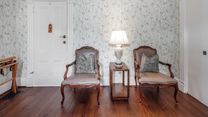 A room with two wooden chairs, a small table with a lamp, and a door with a decorative plate.