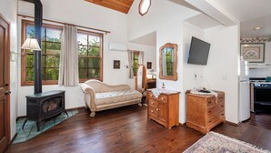 A spacious living room with hardwood flooring, a sofa, a wooden dresser, a television, and a kitchen area. - Bath Street Inn B & B, Santa Barbara (Santa Barbara)