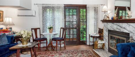 Een woonkamer met een blauwe bank, een houten salontafel, een open haard en een groot raam met gordijnen.