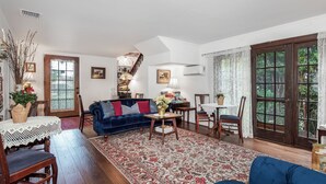A living room with a blue sofa, a wooden coffee table, and a patterned rug. There is a staircase leading to another level, and a large window with curtains. - Bath Street Inn B & B, Santa Barbara (Santa Barbara)