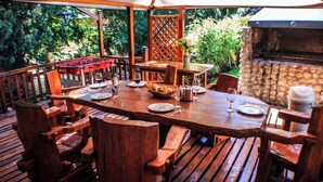 An outdoor wooden deck with a large table set for dining, surrounded by chairs. - Rotui Apart Hotel (San Martín de los Andes)