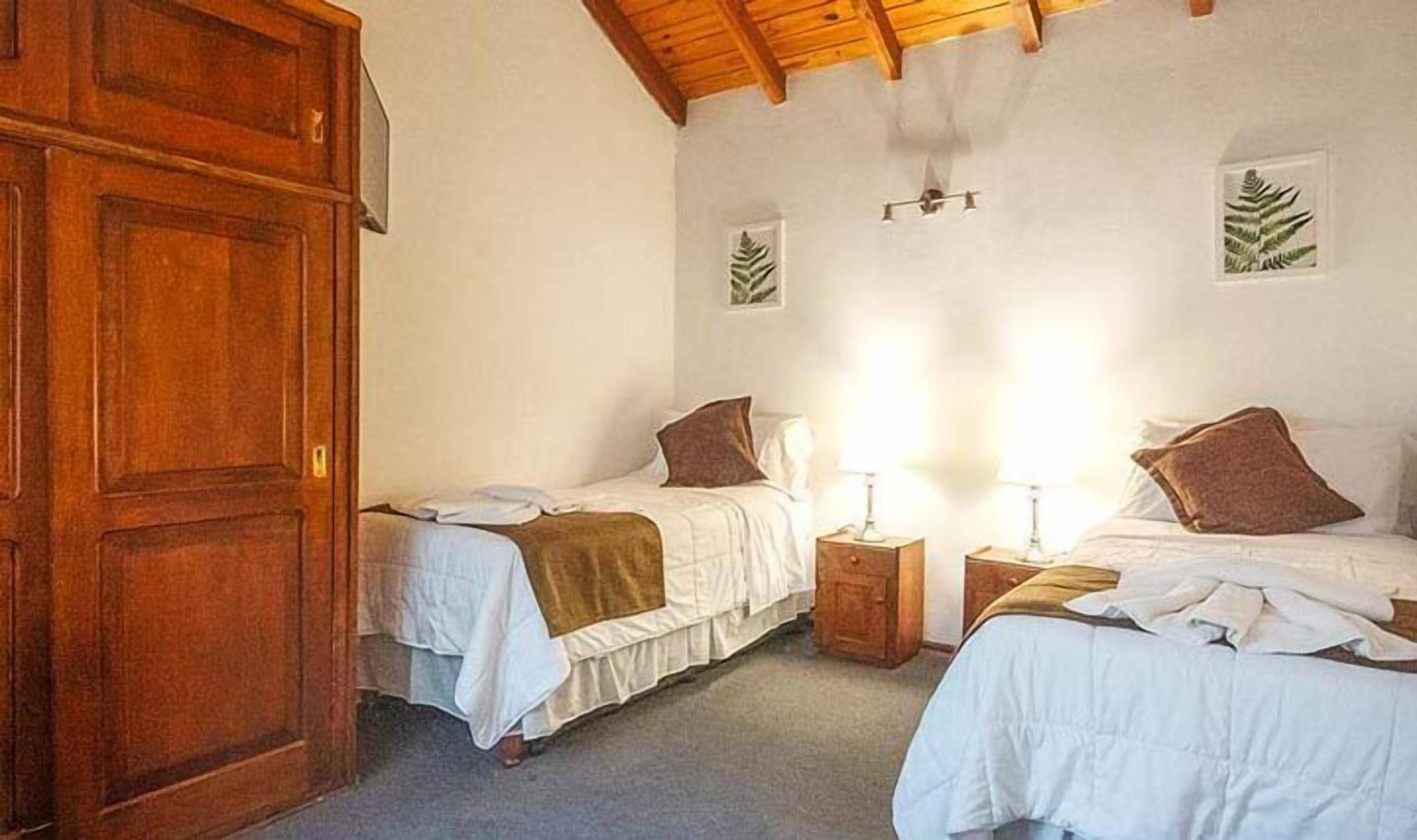 A bedroom with two beds, wooden wardrobe, and a ceiling fan.