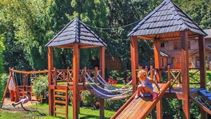 A playground with wooden play structures, including slides and climbing areas, surrounded by greenery. - Rotui Apart Hotel (San Martín de los Andes)