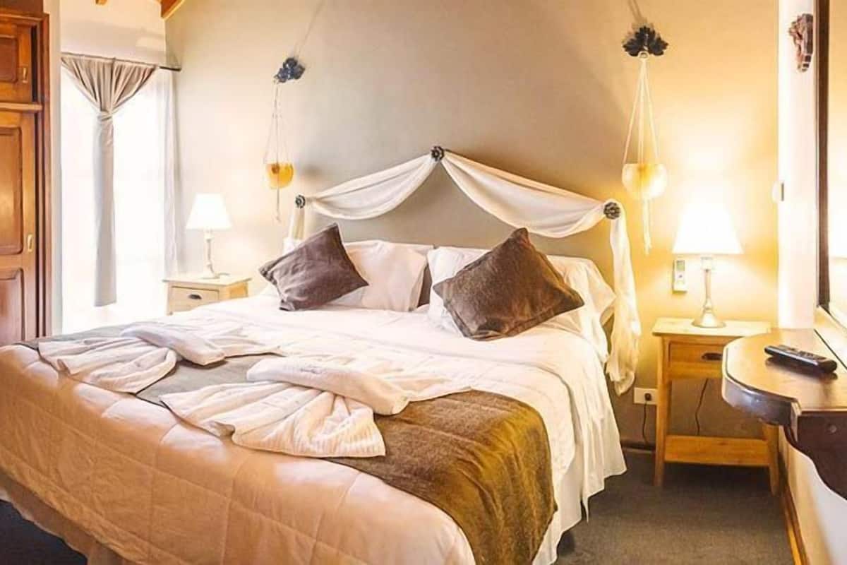 Un lit bien fait, doté d’un baldaquin, une table de chevet avec une lampe et une armoire en bois.