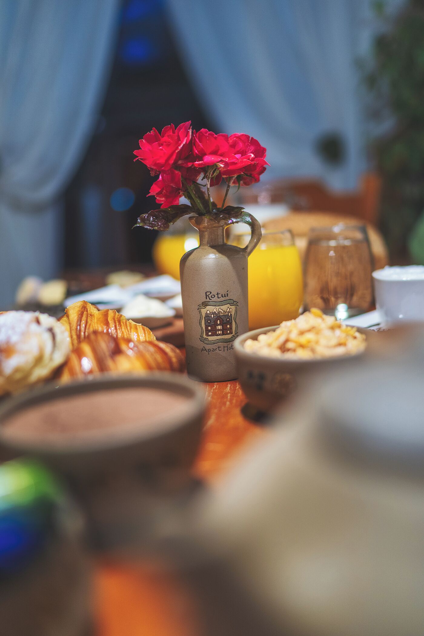 A breakfast table with pastries, a bottle of coffee, and a vase with red flowers.