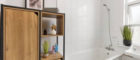 Un baño moderno con una bañera blanca, ducha y un armario de madera con estantes.