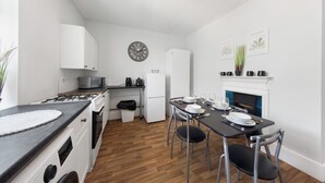A compact kitchen with white appliances, a dining table set for four, and a fireplace. - Modern Getaway in Gillingham (Gillingham)