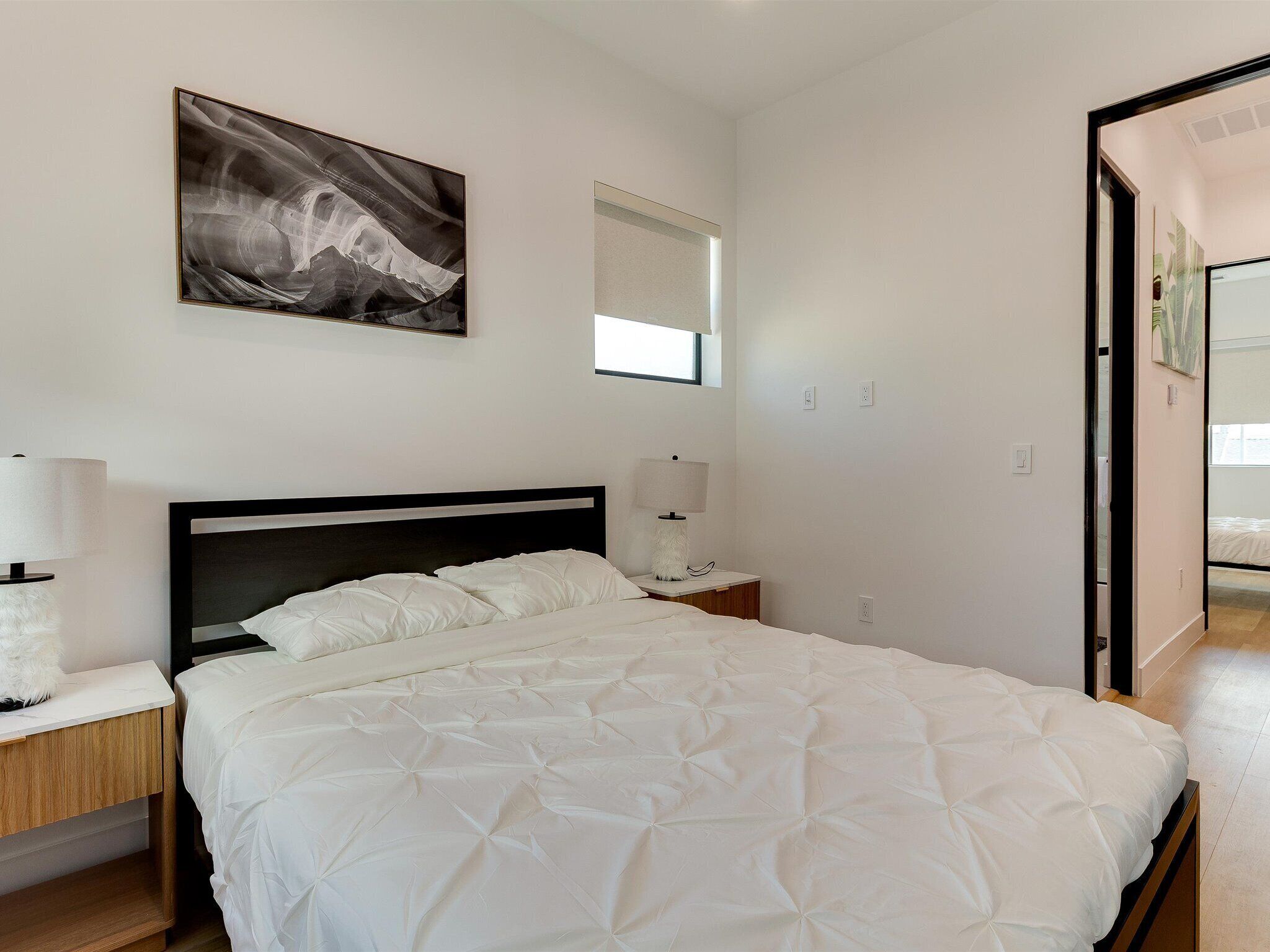 Een slaapkamer met een bed, nachtkastjes, een raam en een schilderij aan de muur.