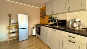 Una cocina moderna con armarios blancos, un refrigerador de acero inoxidable, una cafetera y una pequeña planta en maceta.