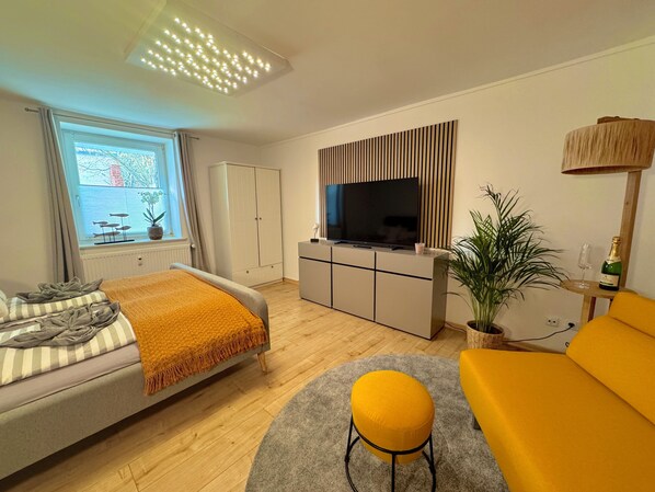 Una sala de estar moderna con un sofá, un televisor, un mueble, una planta y una ventana con cortinas.