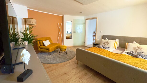 Un dormitorio moderno con una cama, un sofá, una mesita y un televisor.