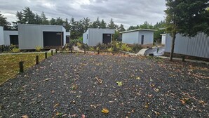 A row of small, single-story buildings with open garage doors, surrounded by gravel and sparse vegetation. - Morning Calm Lodge Limited (Hamilton)