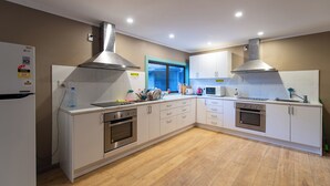 A modern kitchen with white cabinets, stainless steel appliances, and a large window. - Morning Calm Lodge Limited (Hamilton)