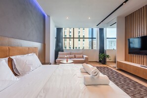 Ein Hotelzimmer mit einem großen Bett, einer Sitzecke, einem Fernseher und Blick auf Gebäude.