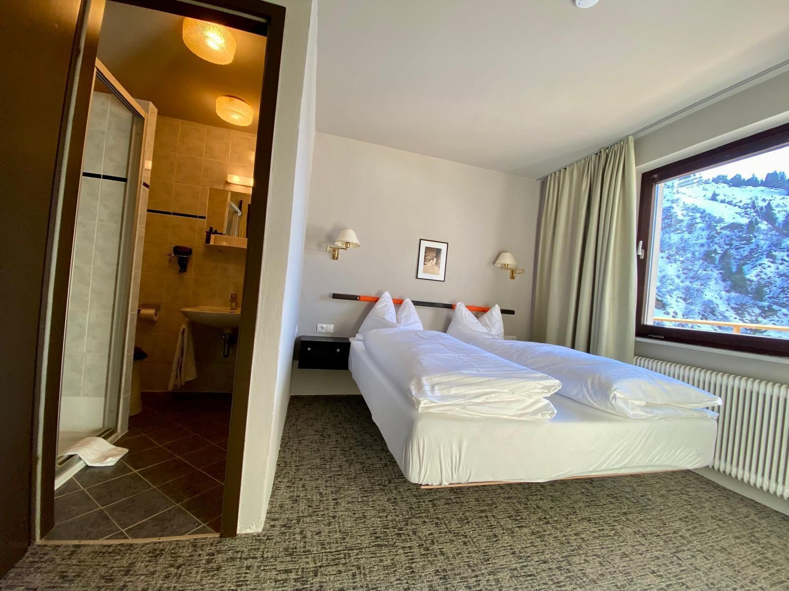 A hotel room with a bed, a window with a view of a snowy landscape, a bathroom, and a mirror.