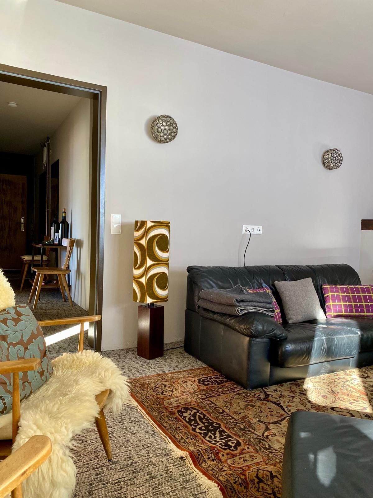 A modern living room with a black leather sofa, patterned rug, and decorative wall pieces.