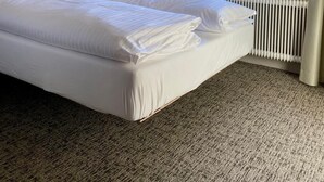 A hotel room with a bed, a window with a snowy mountain view, a radiator, and a wall-mounted lamp. - Arlberg Motel (Klösterle am Arlberg)