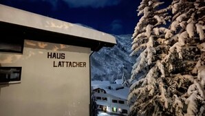 A modern building with the name "HAUS LATTACHER" on its facade, surrounded by snow-covered trees and a mountainous backdrop. - Arlberg Motel (Klösterle am Arlberg)
