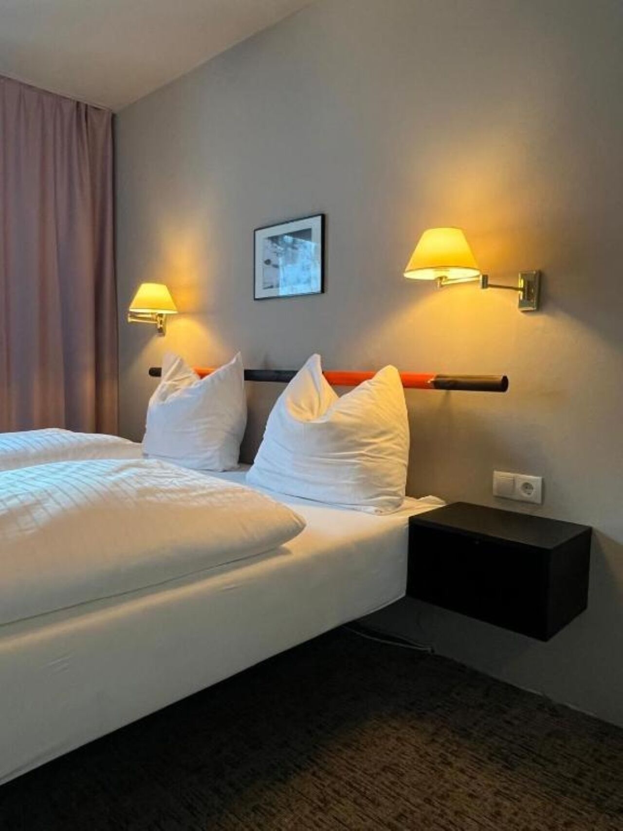 A hotel room with two beds, a nightstand, and two wall-mounted lamps.