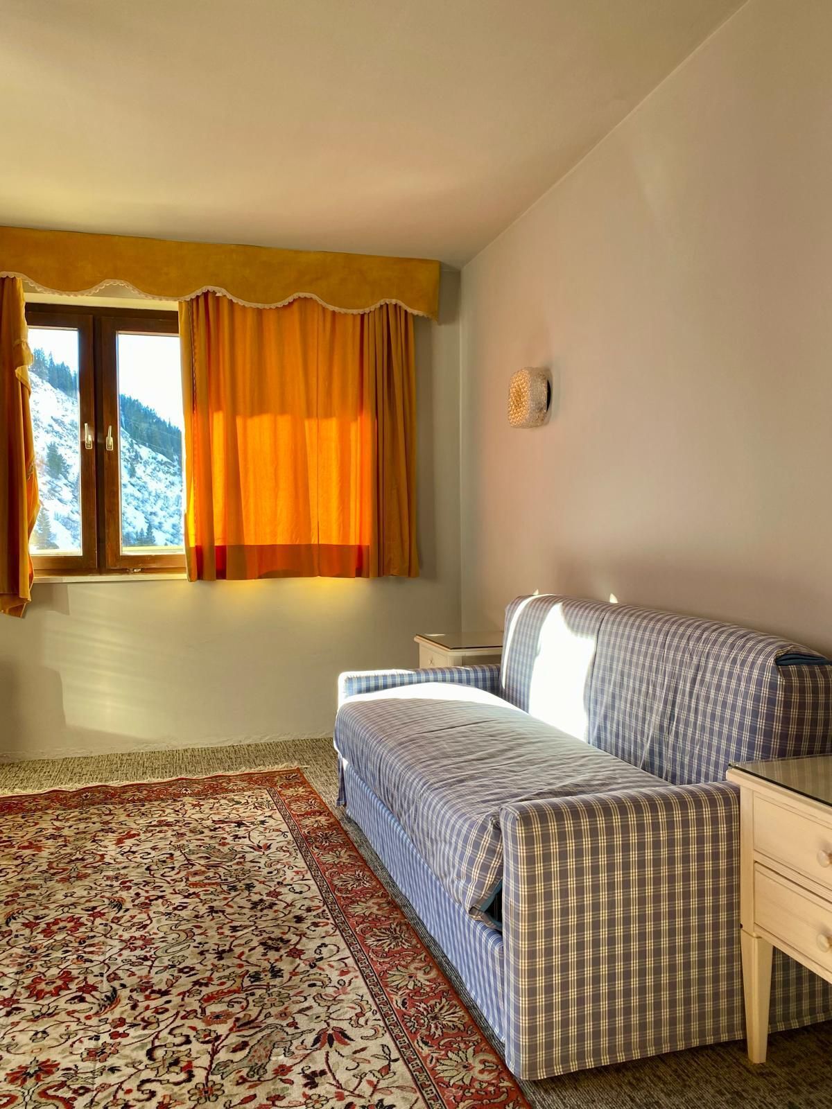 A bedroom with a bed, a nightstand, a window with curtains, and a view of a snowy mountain.