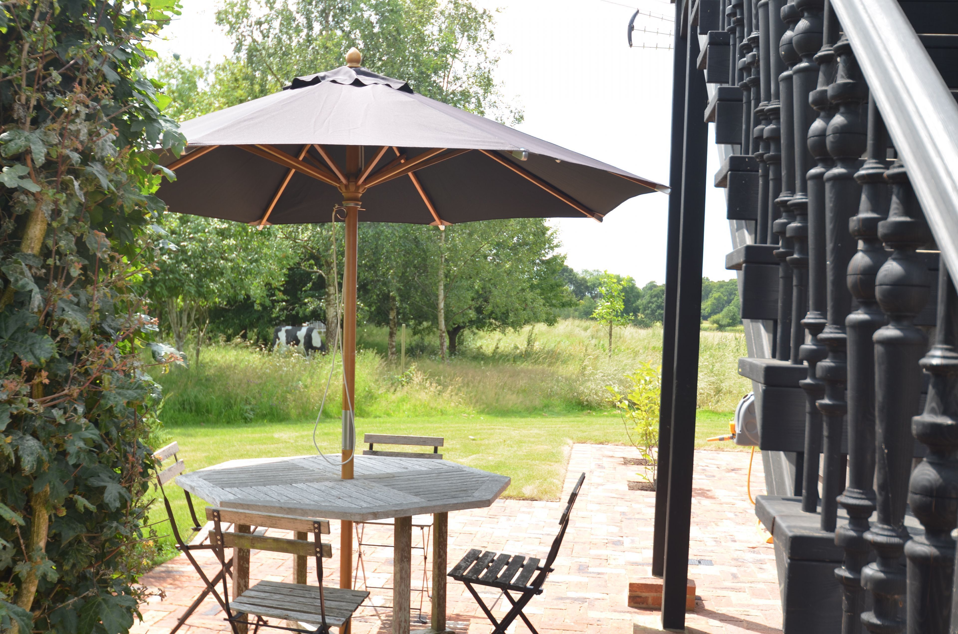 An outdoor patio with a wooden table and chairs, an umbrella, and a brick pathway.