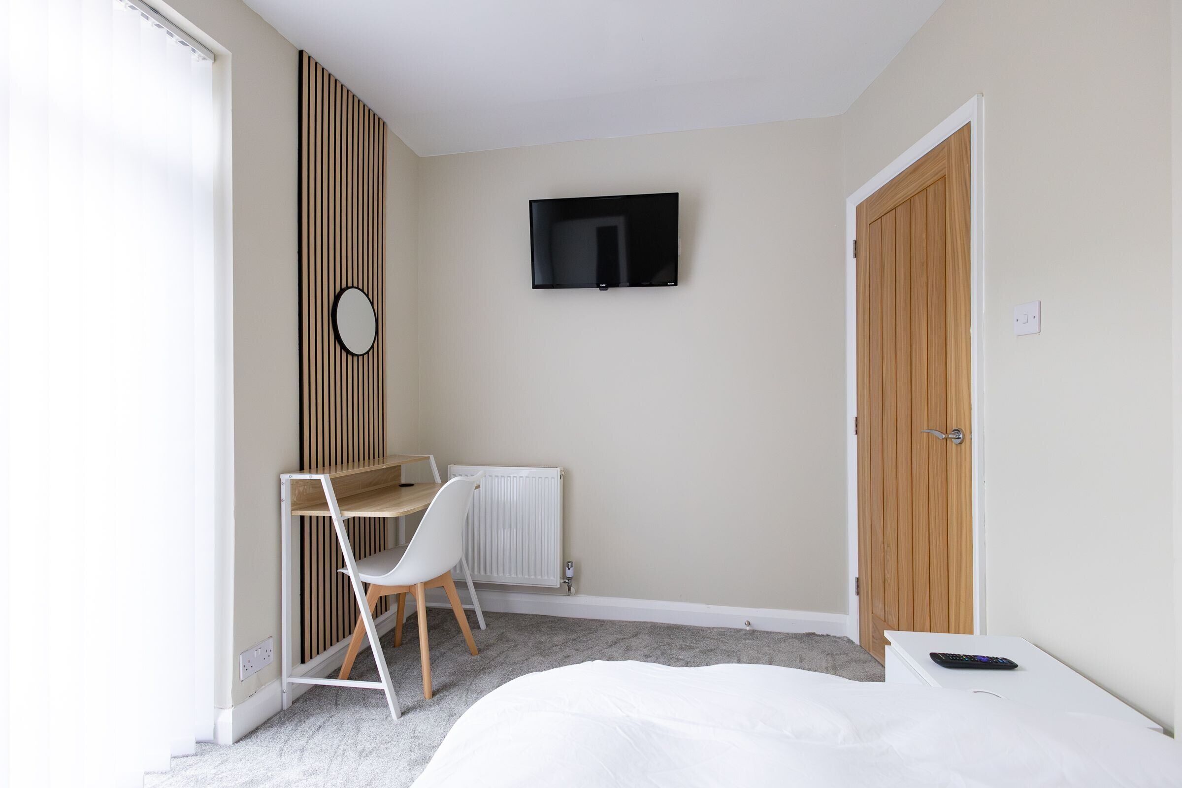 A bedroom with a bed, a desk with a chair, a television mounted on the wall, and a wardrobe.