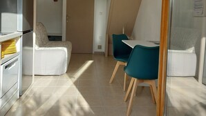 Et moderne køkken med hvide hårde hvidevarer og et spiseområde med turkise stole og et hvidt bord.