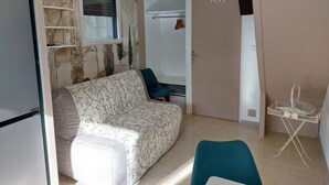 En stue med sofa, stol og et lille bord. En dør fører til et andet rum, og et vindue giver udsigt.
