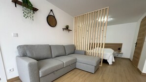 A modern living room with a grey sectional sofa, a wooden slat partition, a small table with a chair, and a wall-mounted clock. - Sublime, cosy and functional studio between braga and gêres (Bico)