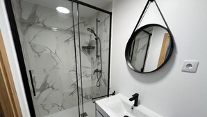 A modern bathroom with a glass shower enclosure, a white sink, and a round mirror. - Sublime, cosy and functional studio between braga and gêres (Bico)