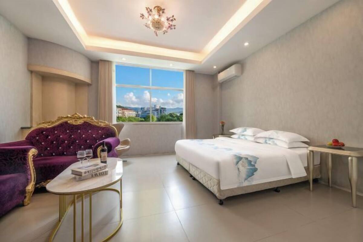 Une chambre d’hôtel avec un lit, un canapé violet, une petite table et une vue sur la ville.
