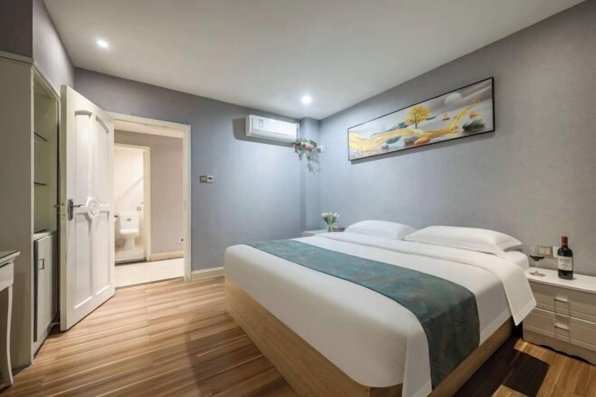 Une chambre à coucher comprenant un lit, une table de chevet, un tableau, un appareil de climatisation et une porte donnant sur une autre pièce.
