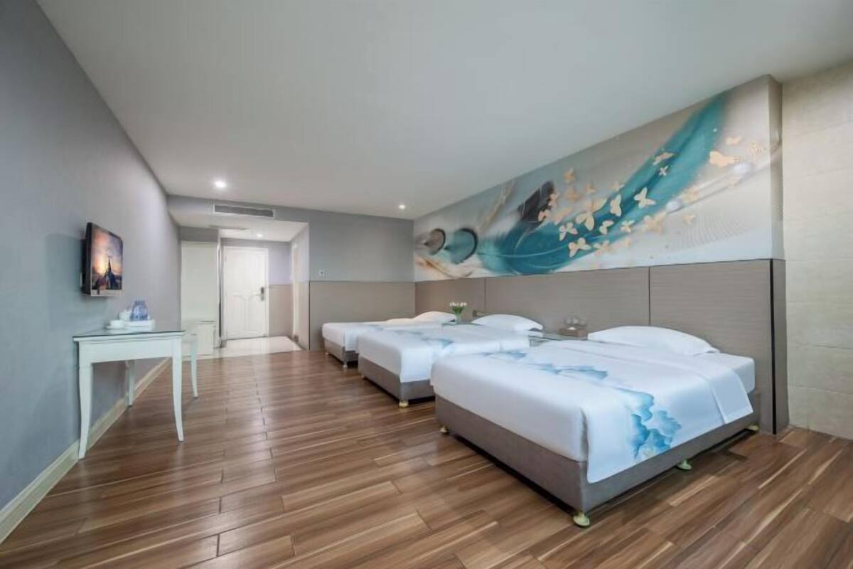 Une chambre d’hôtel avec un plancher en bois, trois lits, un tableau au mur et une petite table.