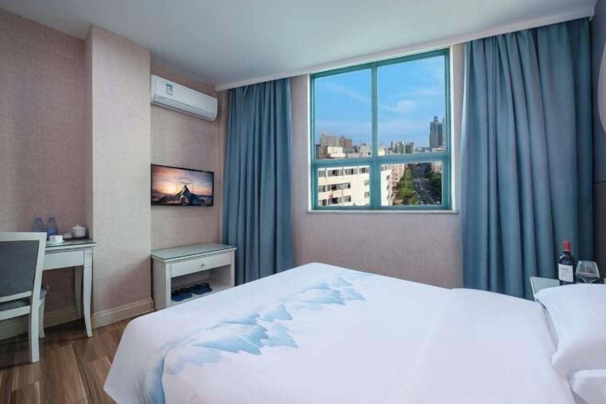 Une chambre d’hôtel avec un lit, un bureau, une chaise, une télévision et une grande fenêtre avec des rideaux.