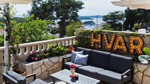 Ulkoterassi, jossa on sohva ja tuoleja, koristeellinen pääveistos sekä kiviseinä, jossa sana ”HVAR” on valaistu.