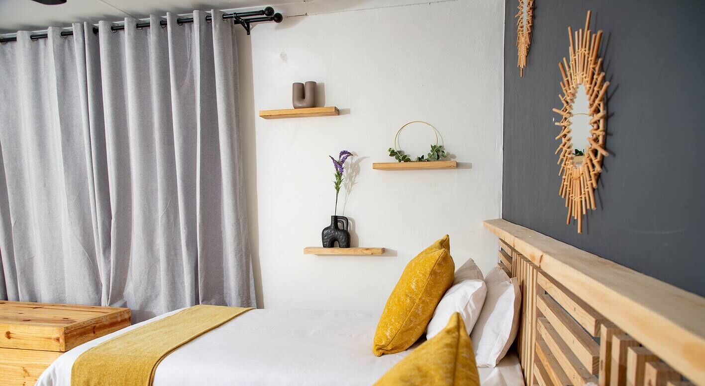 A bedroom with a bed, wooden headboard, gray curtains, and wall-mounted shelves with decorative items.