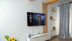 Un salon moderne avec un téléviseur à écran plat fixé au mur, une console blanche, une plante en pot et un rideau gris.