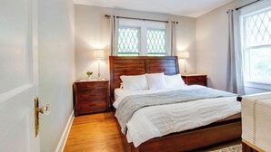 Une chambre à coucher avec un lit en bois, deux tables de chevet, une commode, une fenêtre avec des rideaux et une lampe de chaque côté du lit.