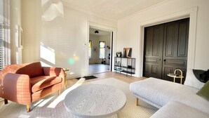 A spacious living room with a large window, a sofa, a coffee table, and a dark wooden door. - Modern Comfort in the Heart of Cherry Hill (Grand Rapids)