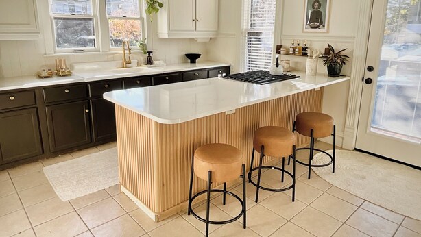 A kitchen with a large island, dark cabinets, white countertops, and a door with a window. - Modern Comfort in the Heart of Cherry Hill (Grand Rapids)