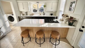 A modern kitchen with a large island, bar stools, a washing machine, and a view of the outside. - Modern Comfort in the Heart of Cherry Hill (Grand Rapids)