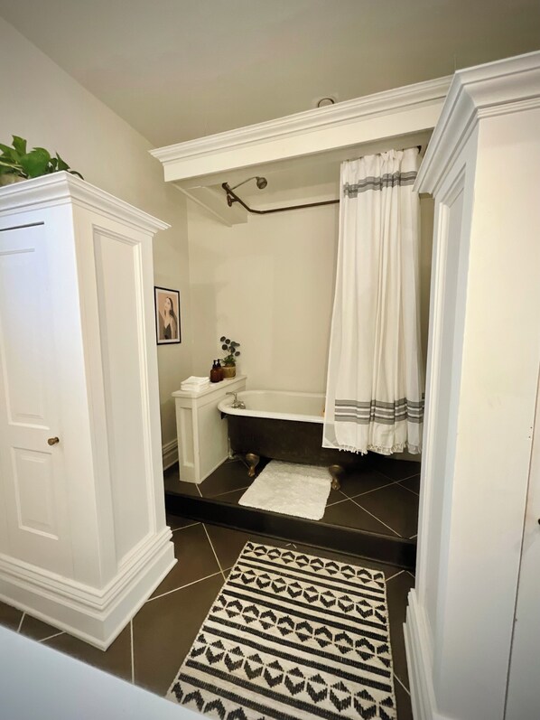 Un baño con bañera, una puerta blanca, una toalla blanca y un tapete estampado.